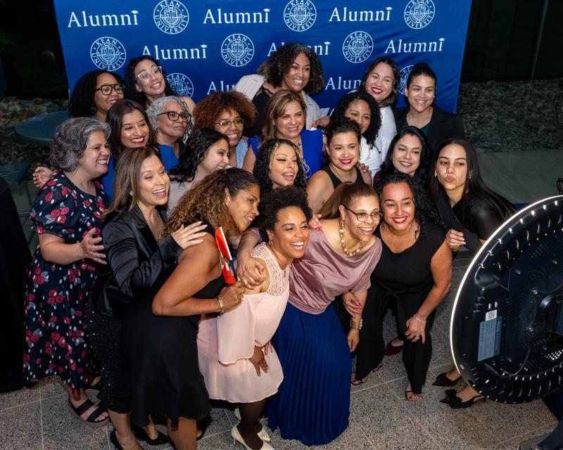 Group of alumni taking a photo in front of a Kean University step and repeat
