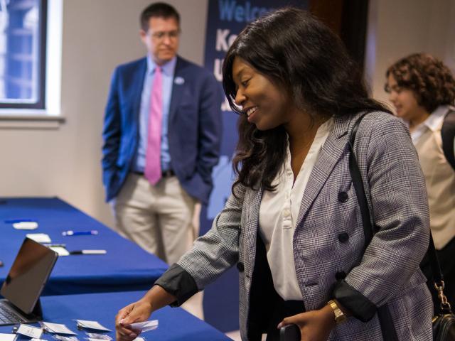 Alumna receiving her name tag  from a table at an alumni event with persons standing in background