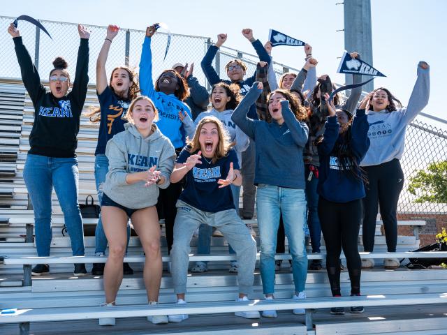 Image of alumni or students shouting exuberantly in the stands for homecoming wearing Kean gear