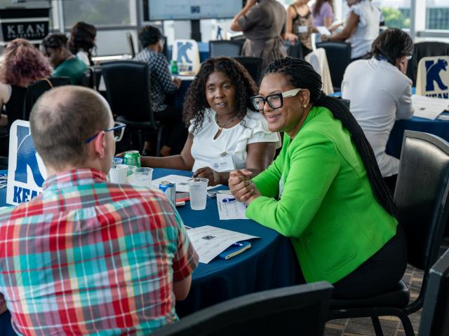 Alumni engaging at a table with Kean logo on table